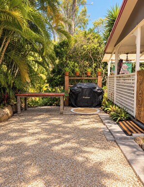 A patio area with a bench, a covered grill, and a white fence with decorative elements.
