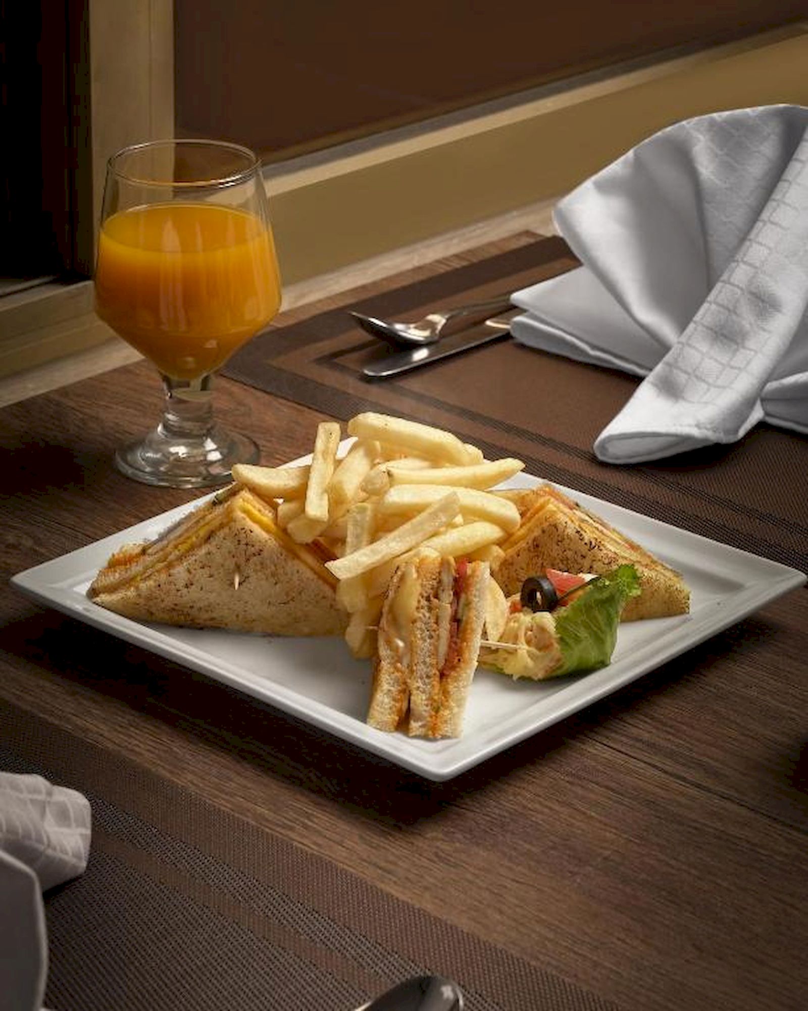 Comida que incluye un sándwich, papas fritas y un vaso de jugo de naranja sobre una mesa.