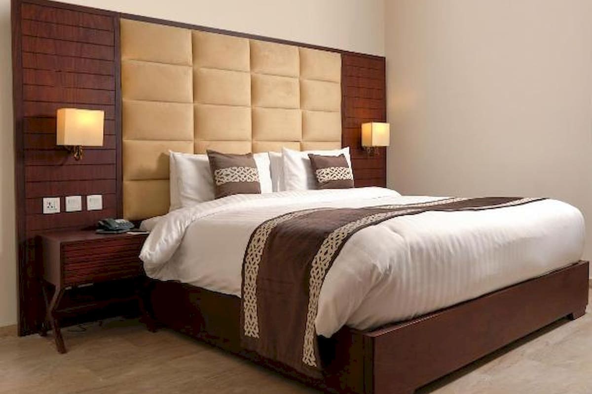 A hotel room with a large bed, wooden headboard, two bedside tables, and wall-mounted lamps.