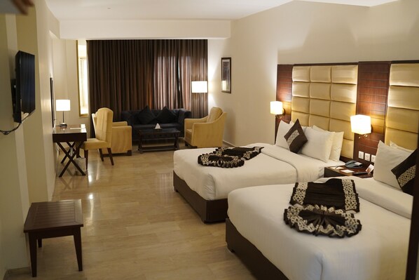 A hotel room with two beds, a sofa, a TV, and a desk.
