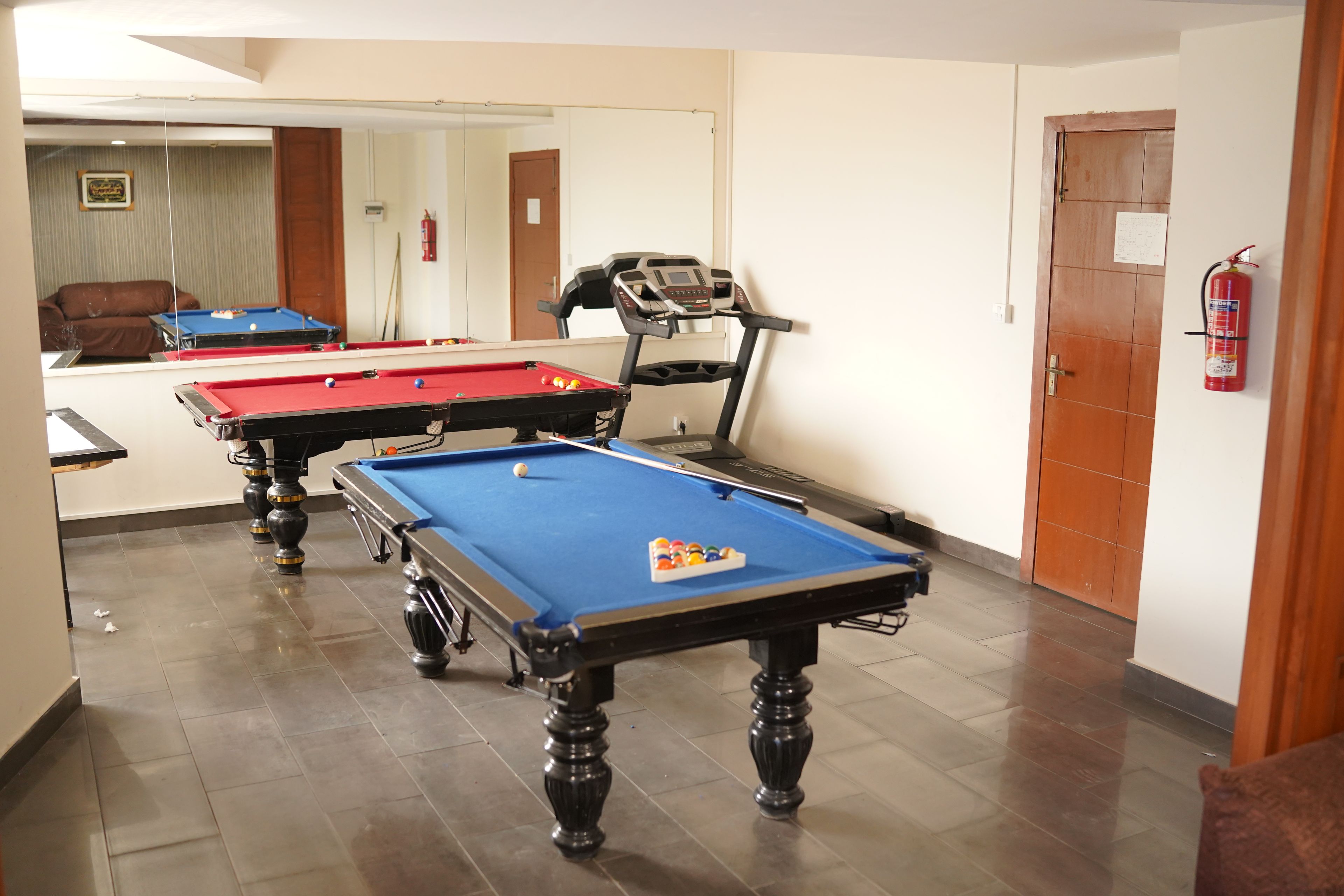 A pool table with a blue felt surface, a red felt table, and a treadmill adjacent to it.