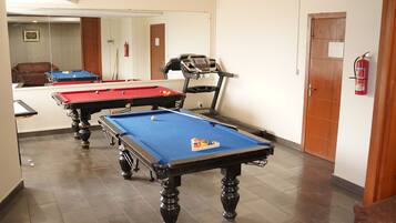 A pool table with a blue felt surface, a red felt table, and a treadmill adjacent to it.