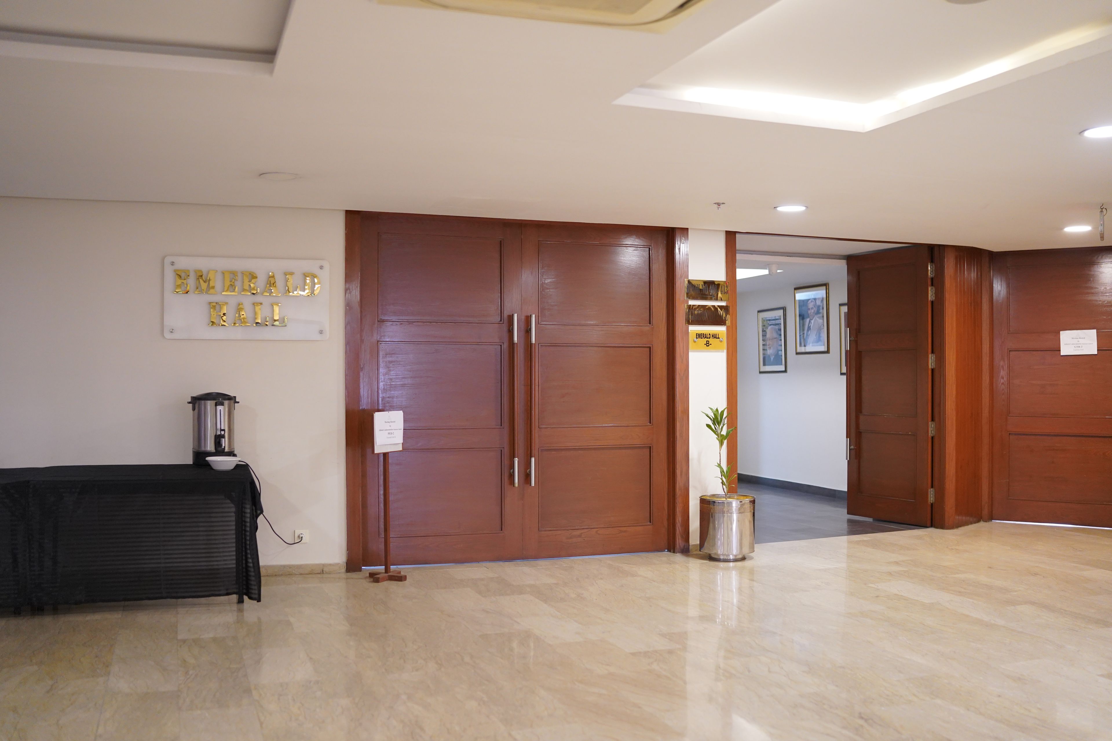 Un vestíbulo de hotel con una máquina de café, un letrero que dice 'Emerald Hall' y una planta en maceta.