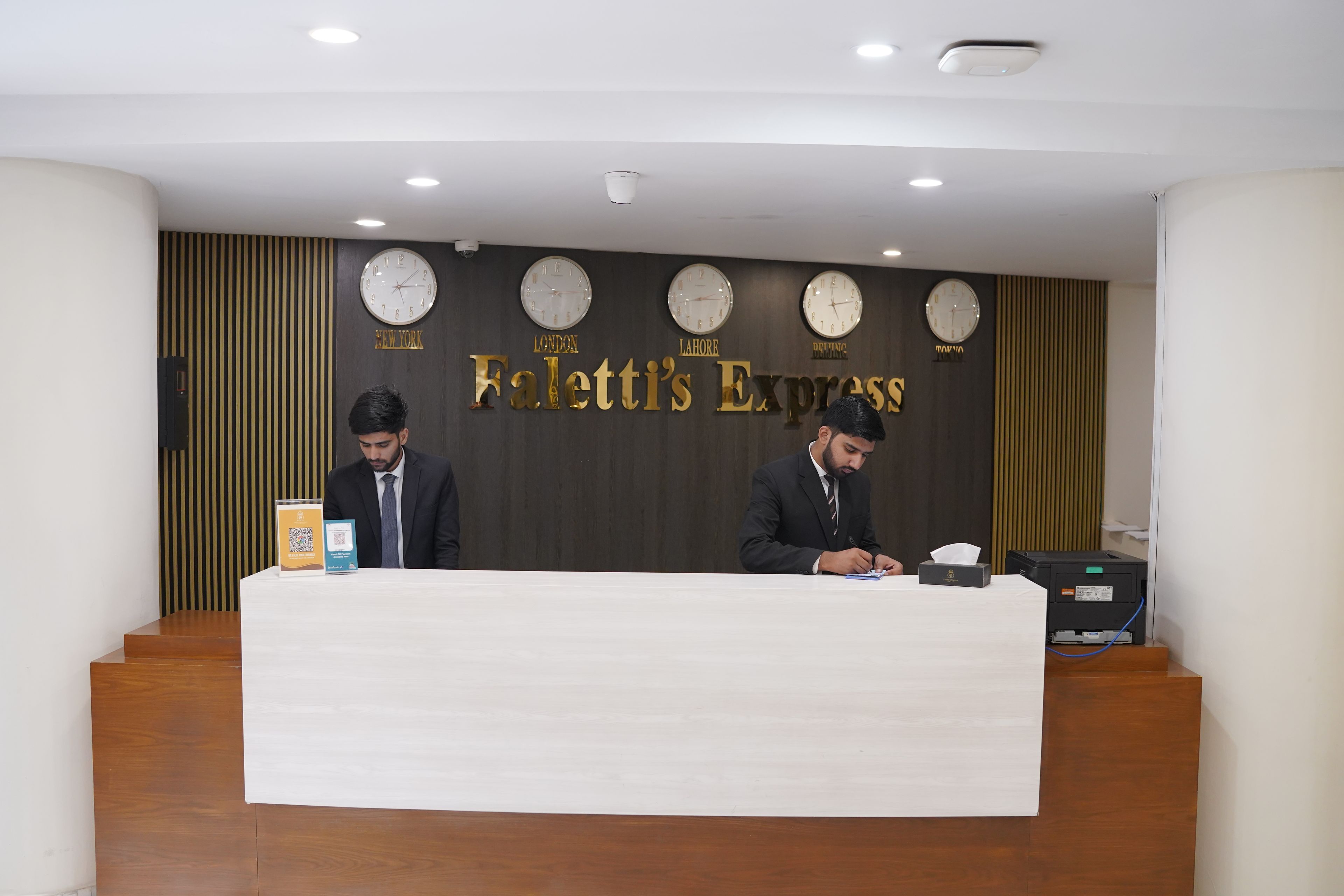 Una recepción con dos empleados, un reloj de pared y un cartel que dice 'Faletti's Express'.