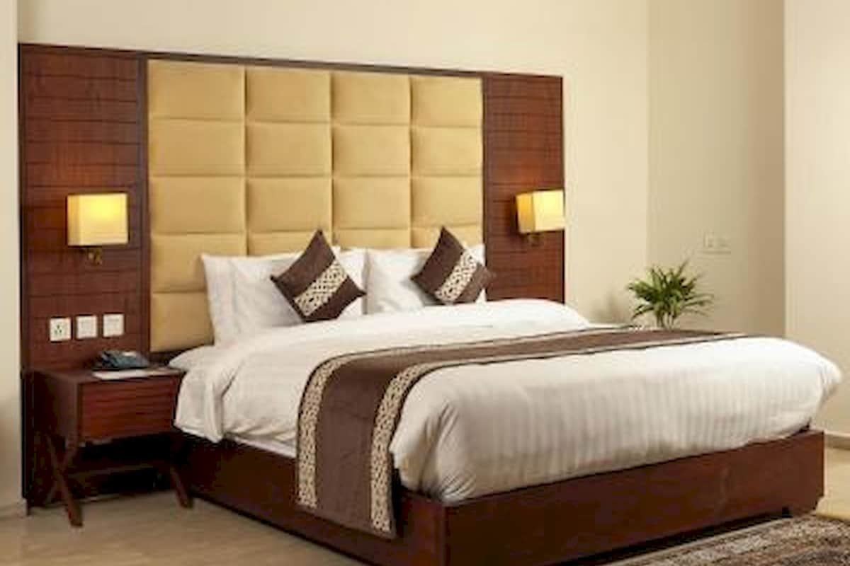 A hotel room with a large bed, wooden headboard, bedside lamps, and a small plant.