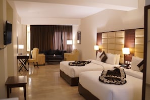 A hotel room with two beds, a desk, a chair, a sofa, and a television.