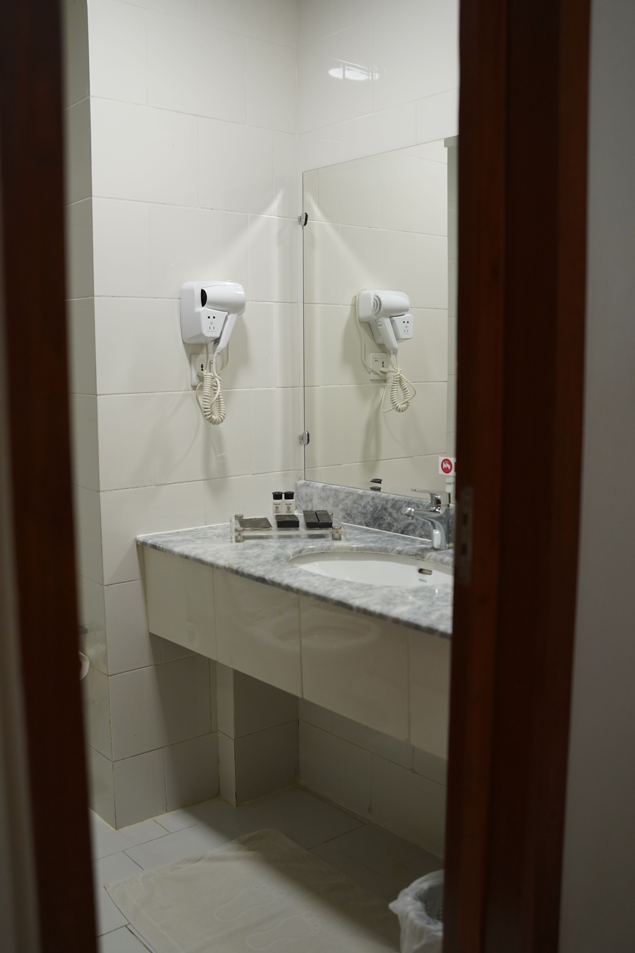 A bathroom with white tiles, a marble sink, and two hair dryers mounted on the wall.
