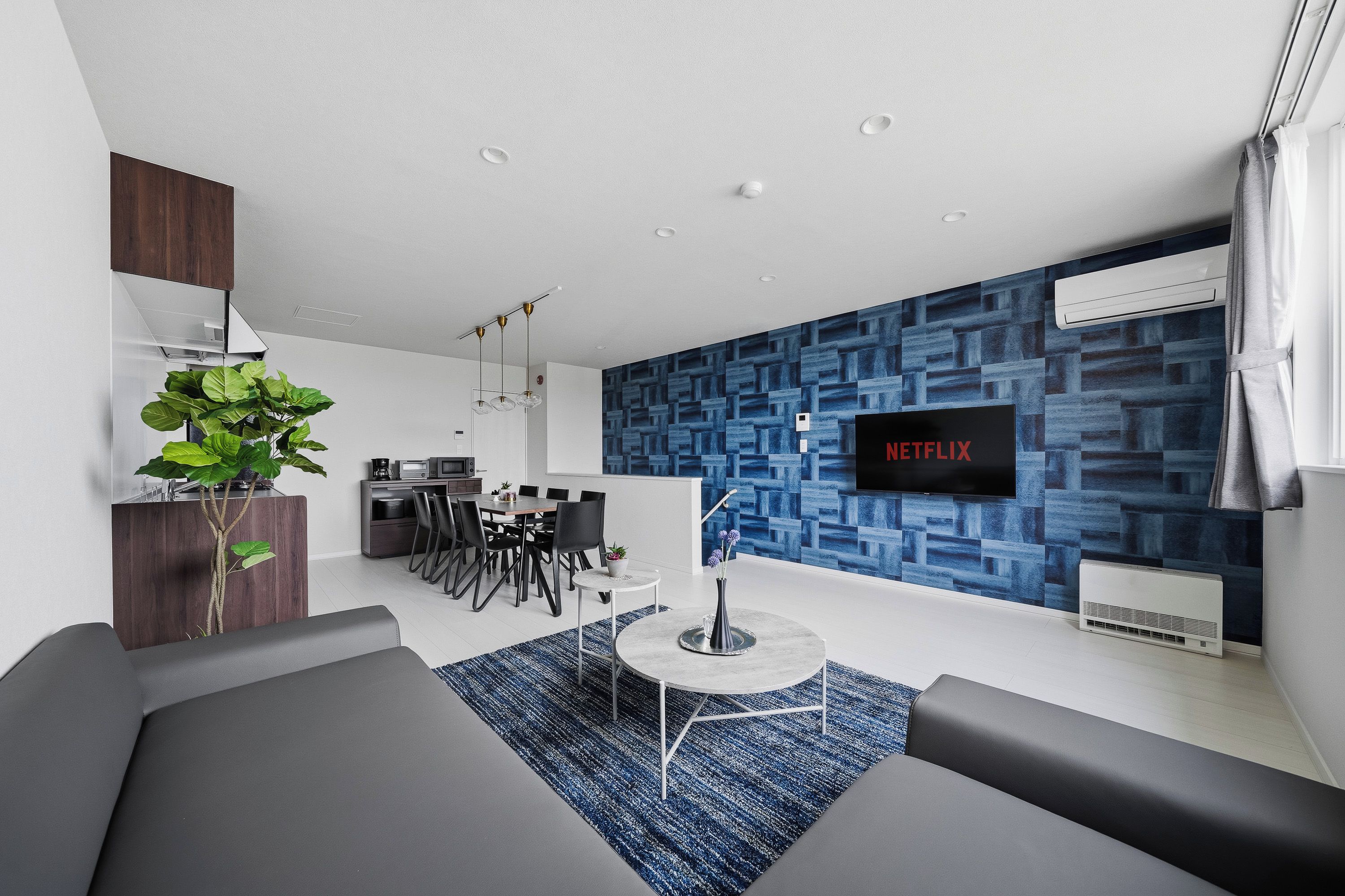 A modern living room with a flat-screen TV, a dining area, and a kitchen.