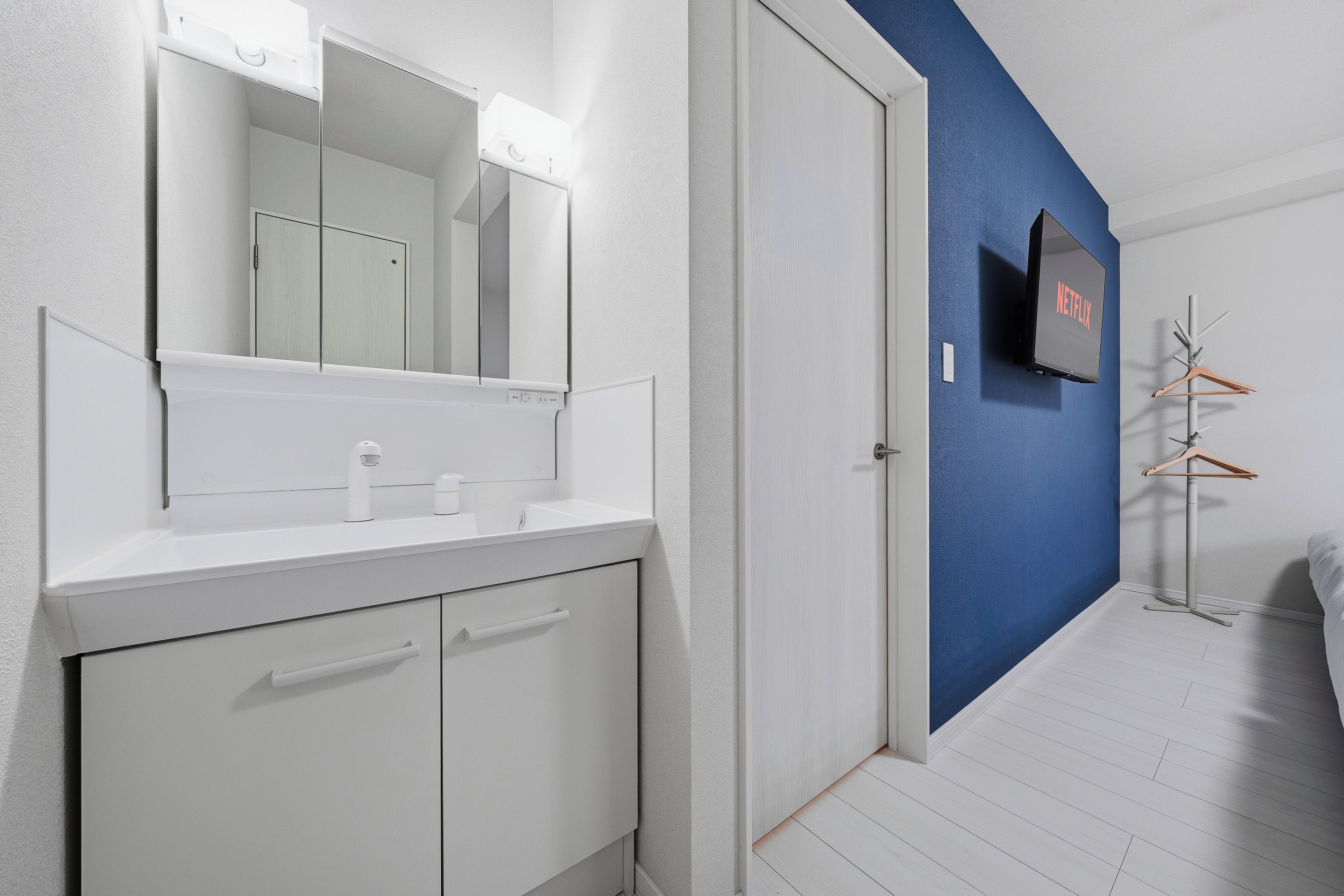 A modern bathroom with a white vanity, a mirror, and a wall-mounted TV displaying the Netflix logo.