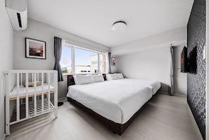 A bedroom with a crib, a bed, a window with curtains, and a wall-mounted TV. - Snow (Furano)