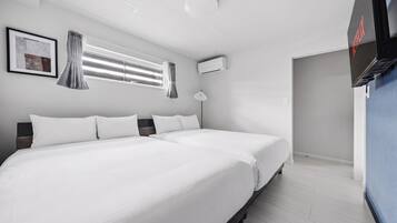 A hotel room with two beds, a window with blinds, an air conditioning unit, and a television.