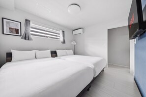 Et hotelværelse med to senge, et vindue med rullegardiner, en aircondition og et fjernsyn.