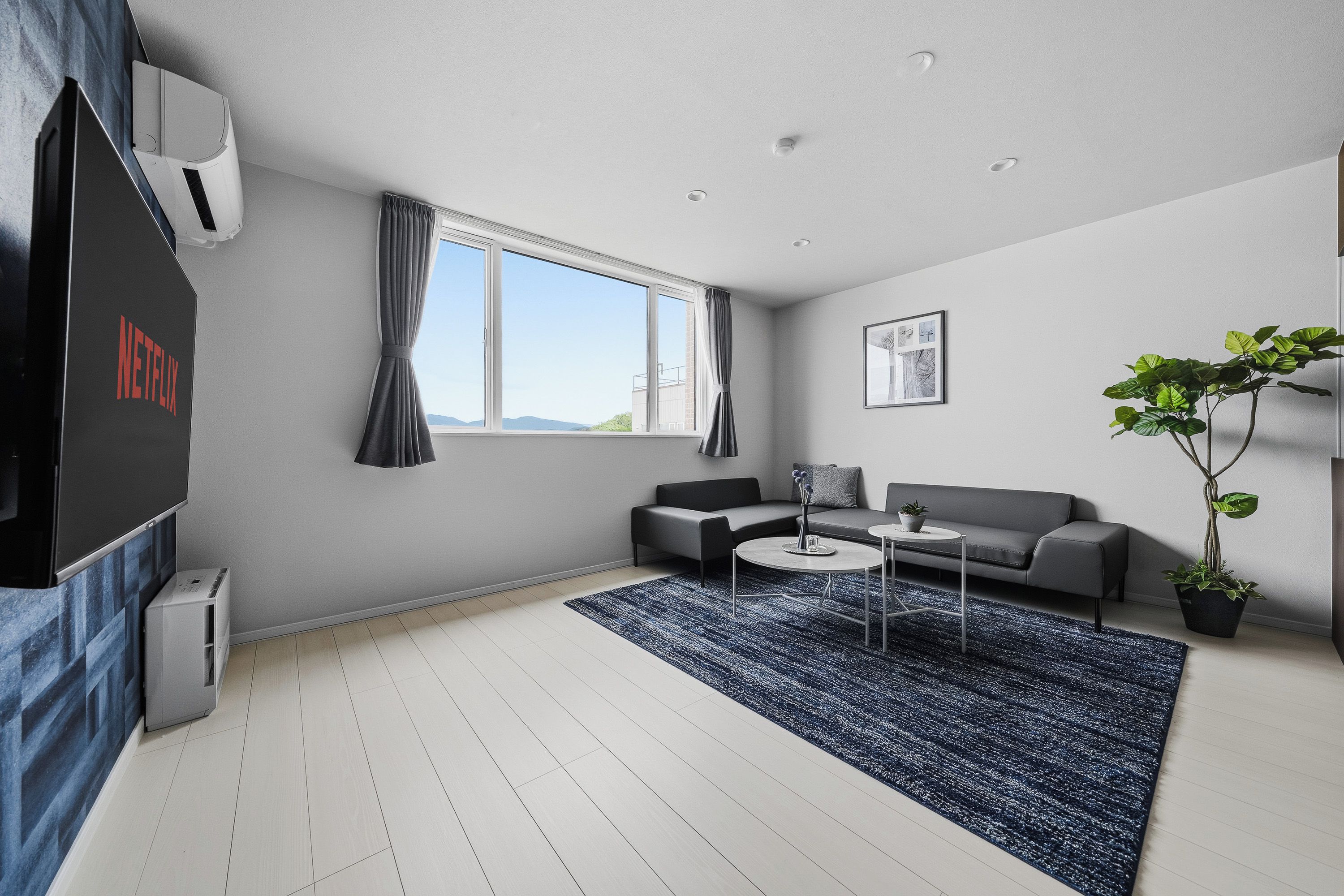 A modern living room with a grey sofa, a coffee table, a TV, and a large window with curtains.