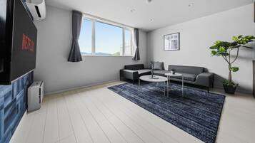 A modern living room with a grey sofa, a coffee table, a TV, and a large window with curtains.