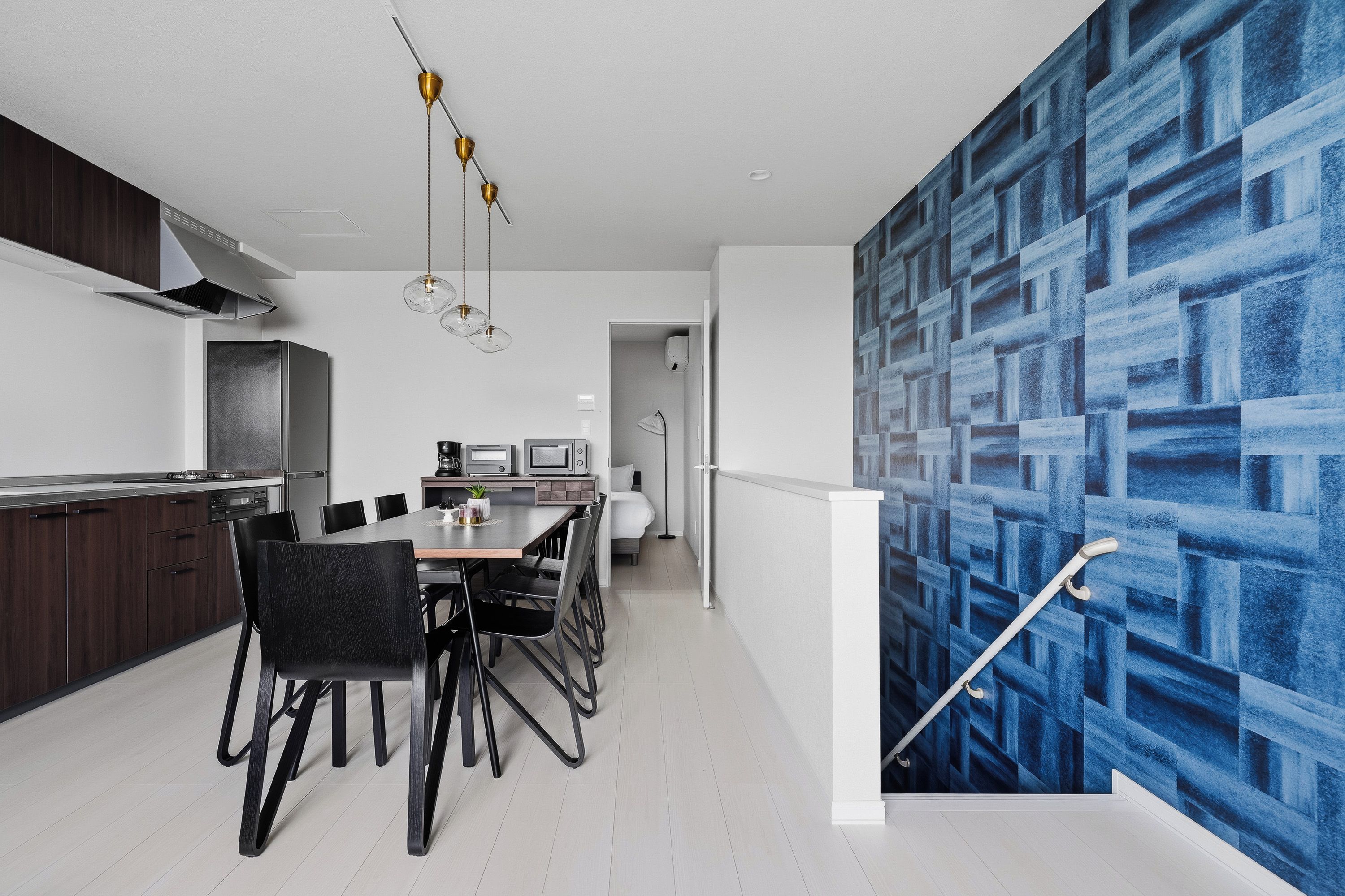 A modern kitchen with a dining area, a staircase, and a blue patterned wall.