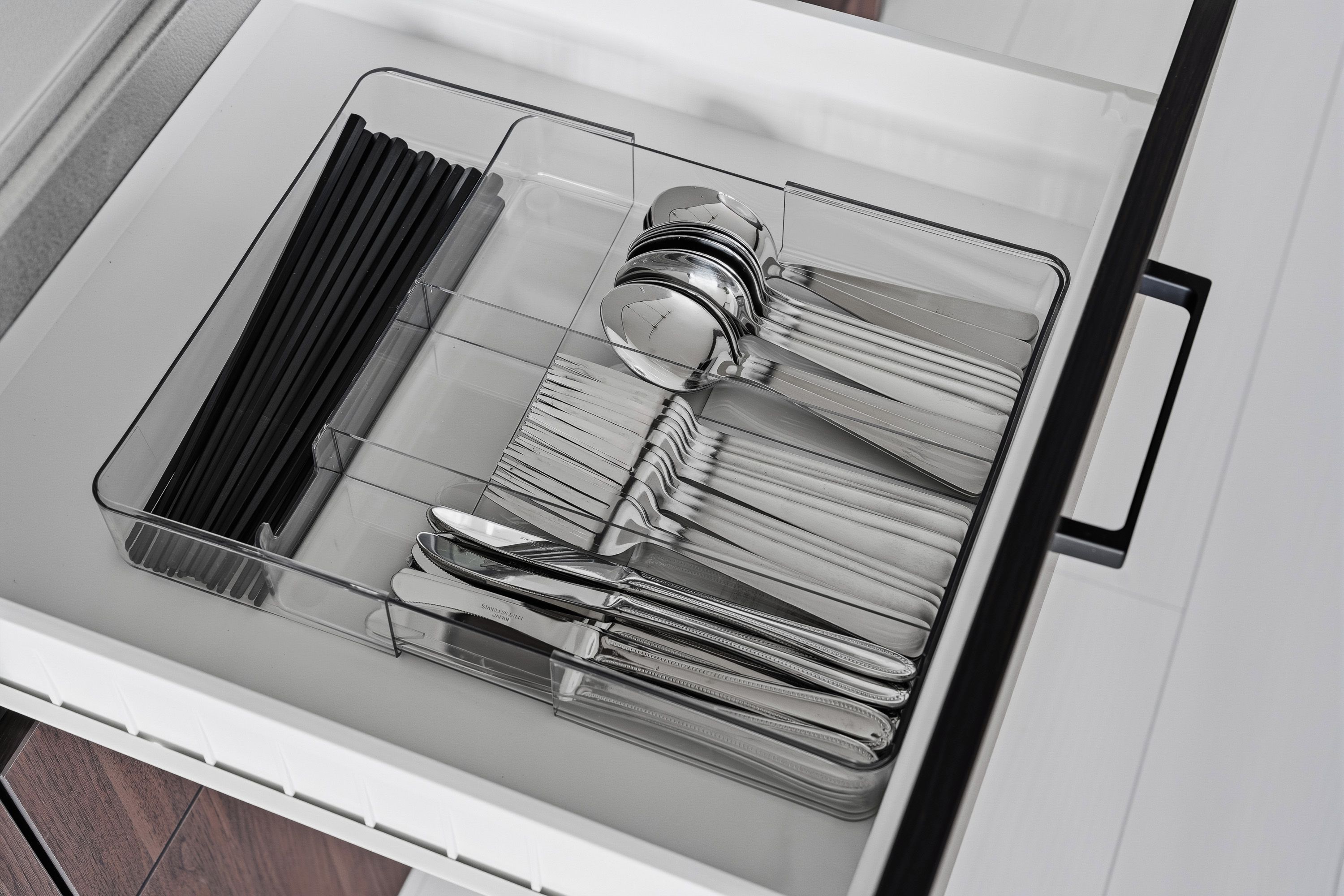 A drawer with a clear organizer containing stainless steel cutlery and a glass container.