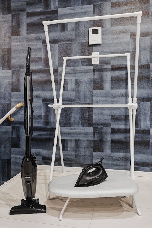 A room with a vacuum cleaner, an ironing board, and a white stand with a control panel. - Snow (Furano)