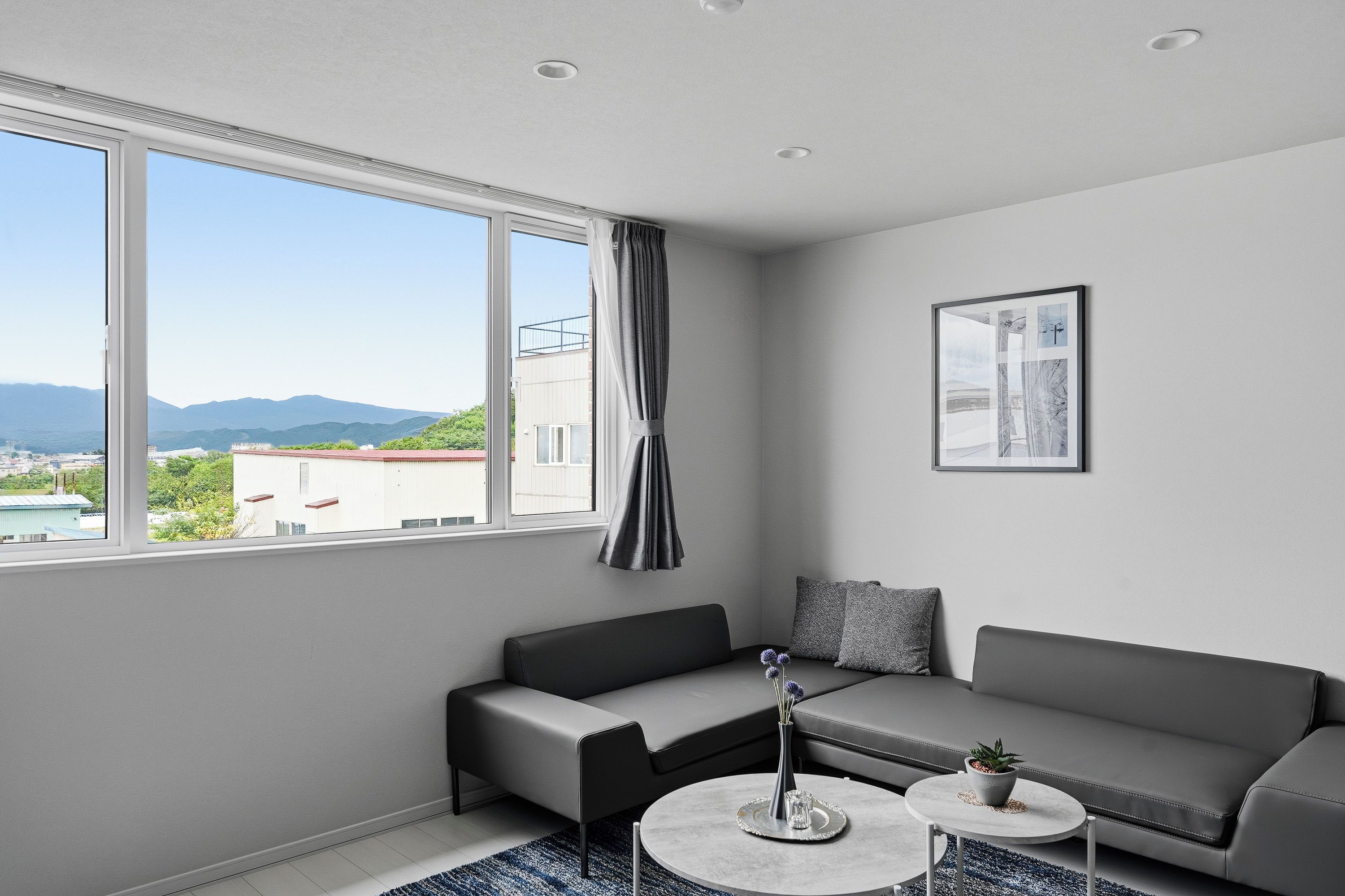 Un salon moderne avec un canapé, une table basse et une vue sur le paysage urbain grâce à de grandes fenêtres.