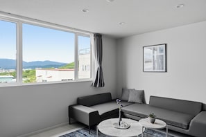 A modern living room with a sofa, a coffee table, and a view of the cityscape through large windows. - Snow (Furano)