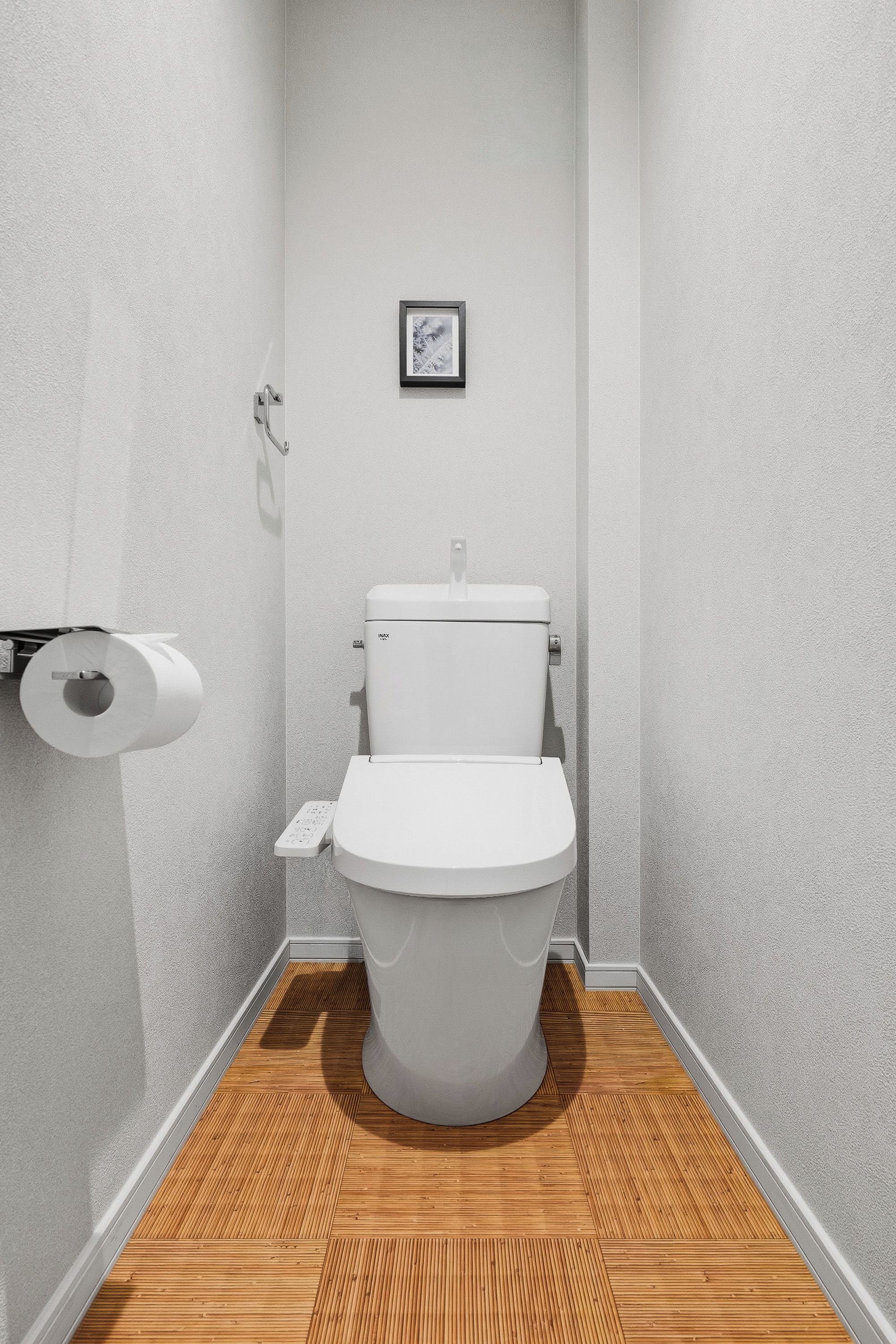 Un baño con un inodoro, un rollo de papel higiénico y un cuadro en la pared.