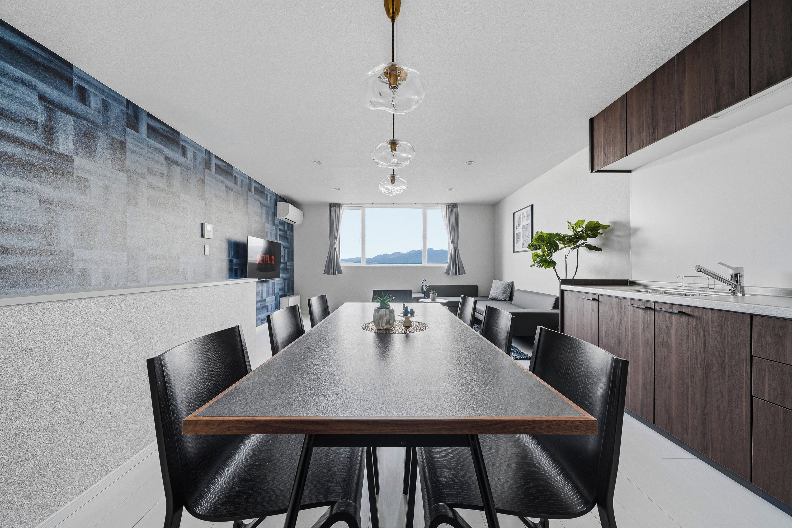 Un espace repas moderne avec une longue table, des chaises noires et une vue sur l’extérieur.