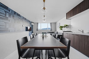 A modern dining area with a long table, black chairs, and a view of the outdoors. - Snow (Furano)