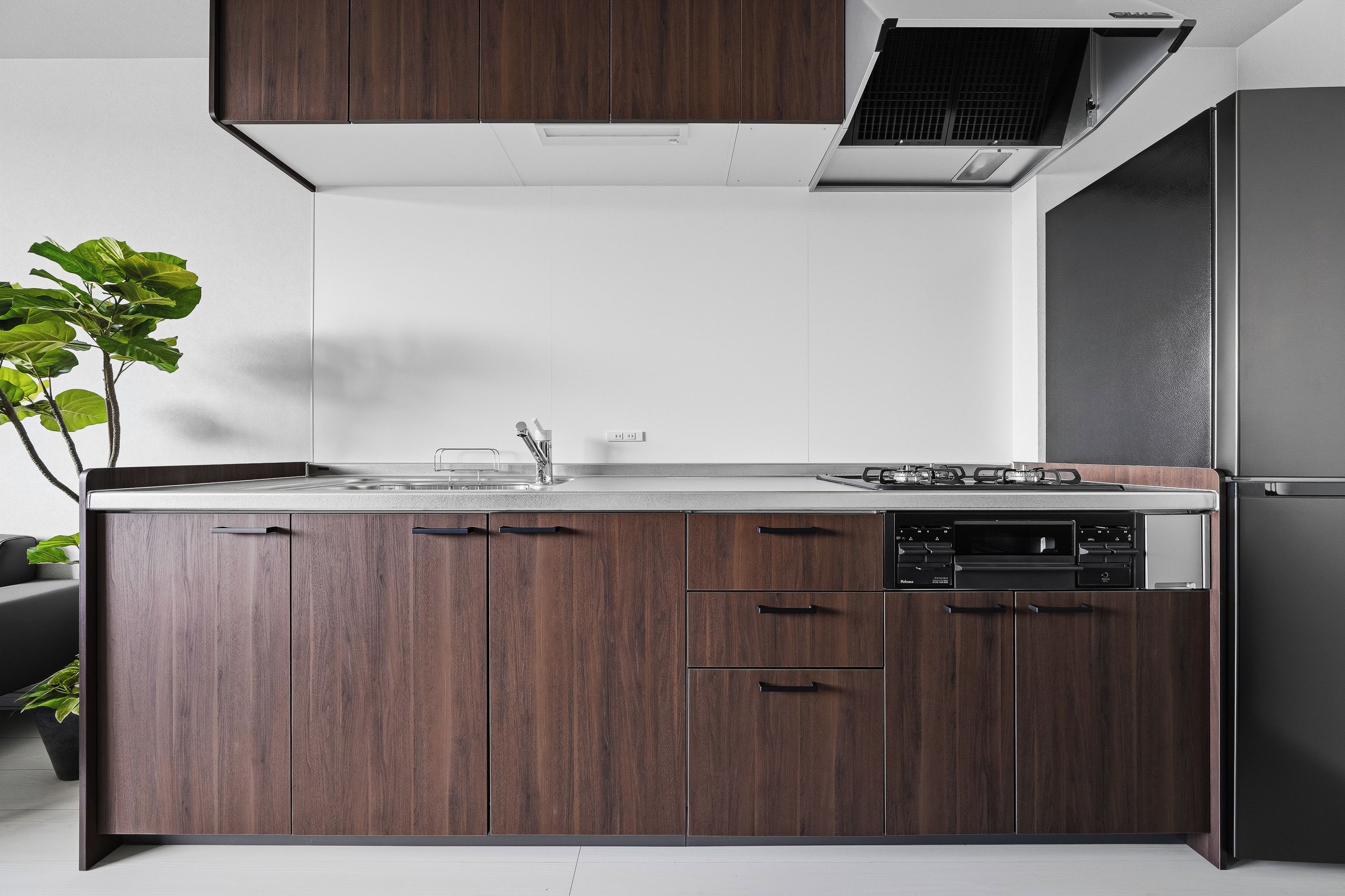 A modern kitchen with dark wood cabinets, a stainless steel sink, and a built-in dishwasher.