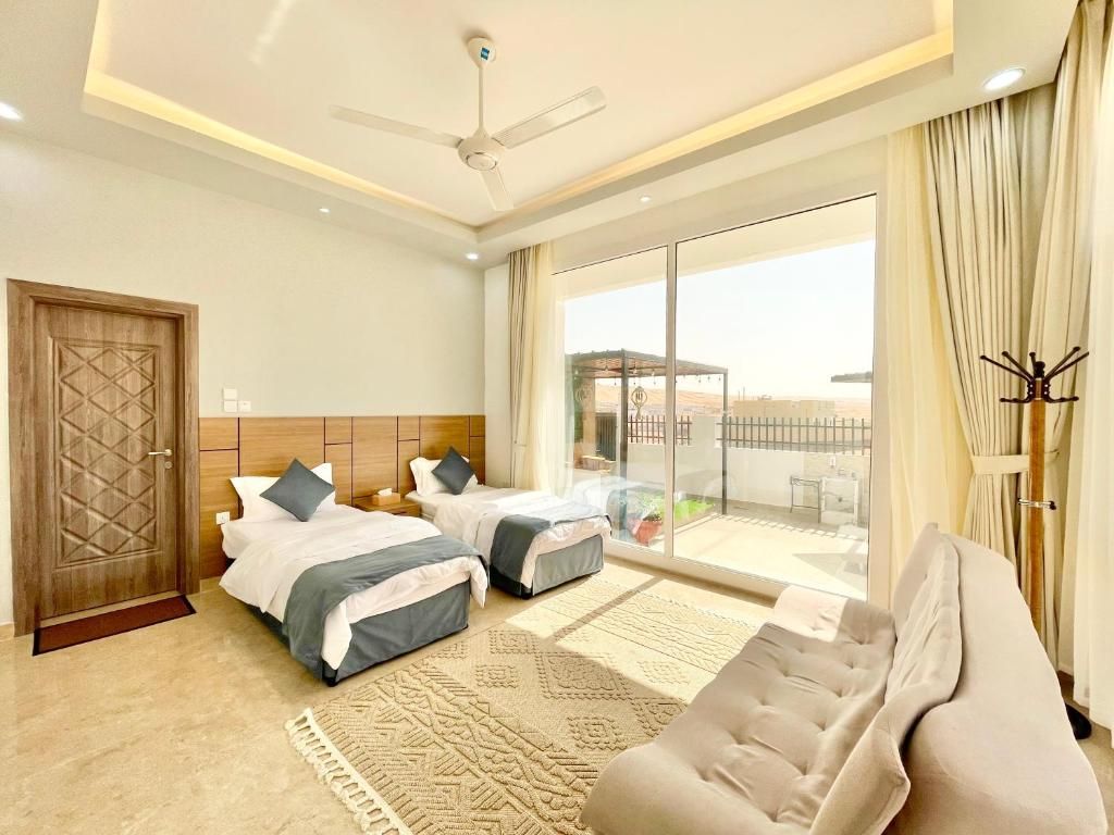 A hotel room with two beds, a sofa, a ceiling fan, and a view of the outside.