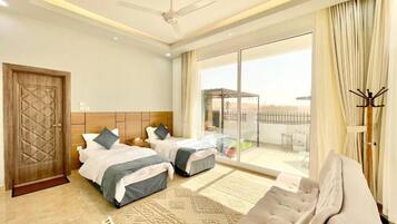 A hotel room with two beds, a sofa, a ceiling fan, and a view of the outside.