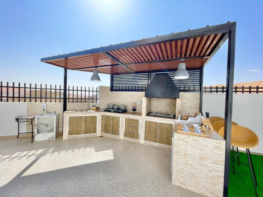 Cozinha externa com churrasqueira integrada, pia e área de bar com banquetas.
