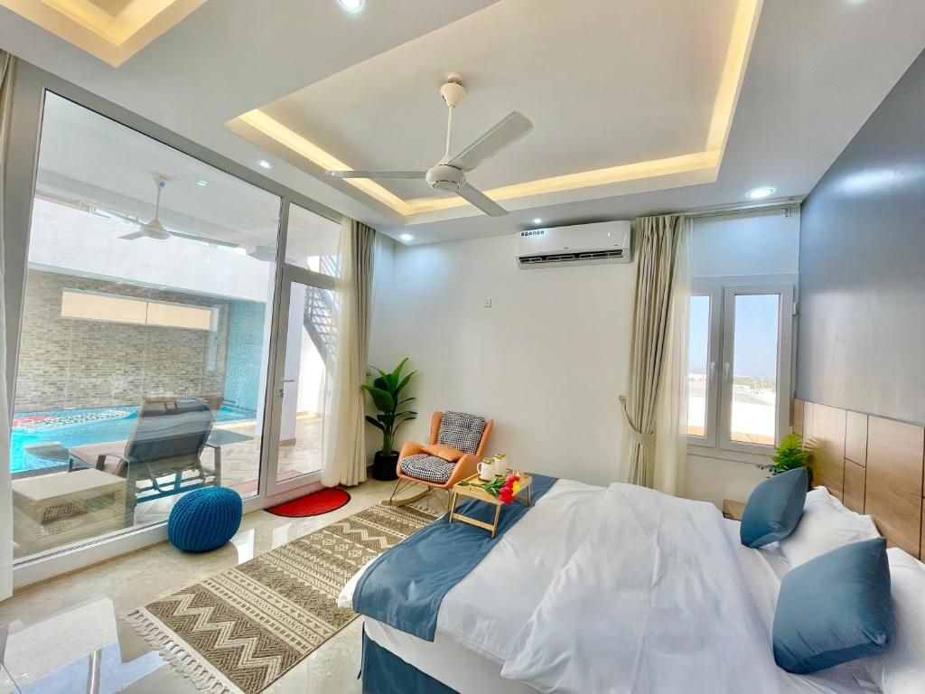 Habitación de hotel con cama, escritorio, silla, una mesita con una planta y vista a una piscina.