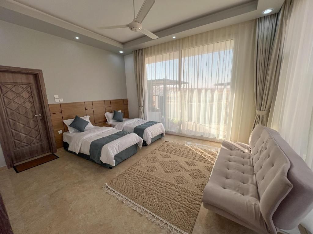 A hotel room with two beds, a sofa, a ceiling fan, and a large window with curtains.