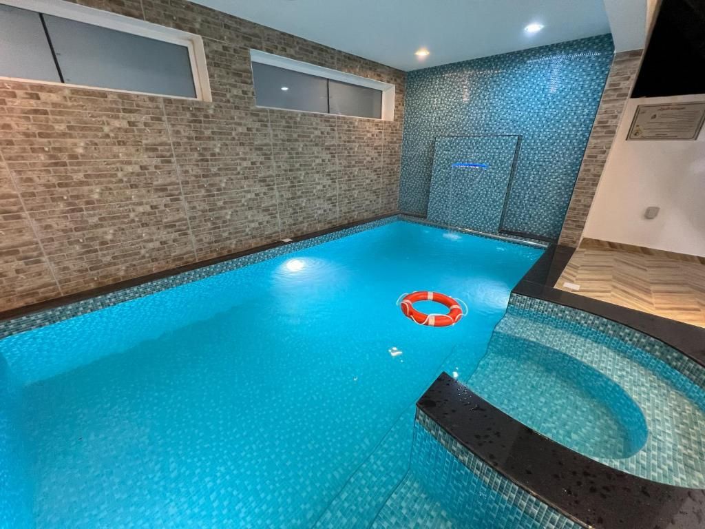 Une piscine intérieure à l’eau d’un bleu limpide, équipée d’une bouée de sauvetage et dont un des murs est recouvert de carreaux, avec une fenêtre.