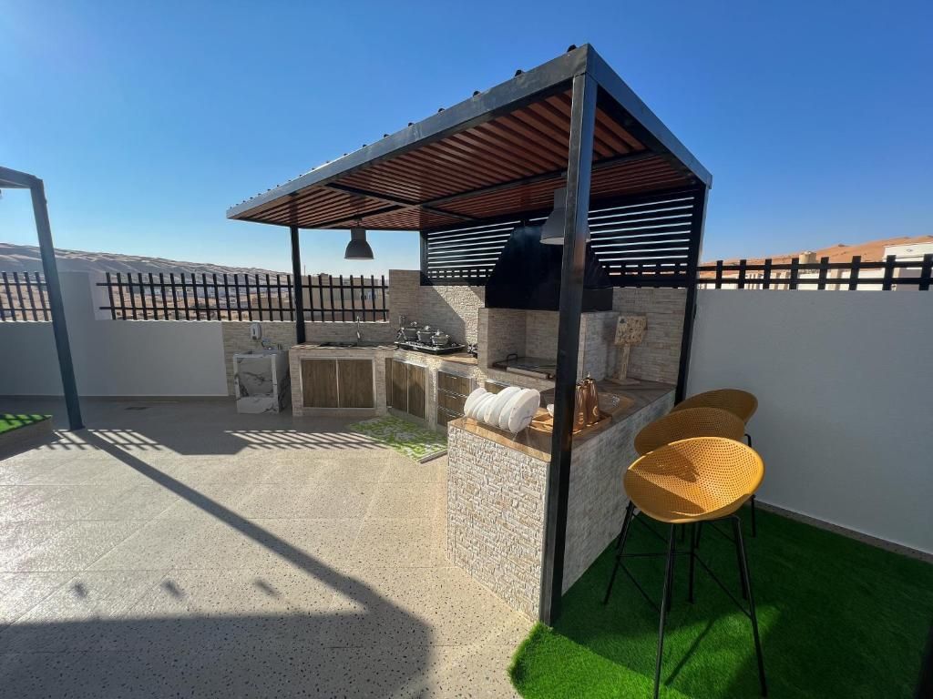 Een terras buiten met een barbecueplek, zitplaatsen en een pergola.