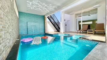 An indoor swimming pool with clear blue water, a brick wall, and a staircase leading to an upper level.