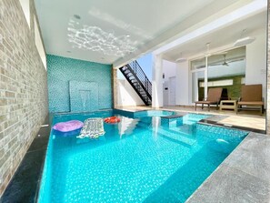An indoor swimming pool with clear blue water, a brick wall, and a staircase leading to an upper level.