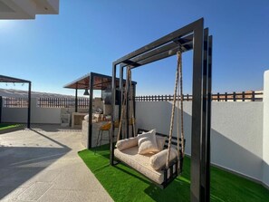 A modern outdoor seating area with a swing chair, a small table, and a chair.