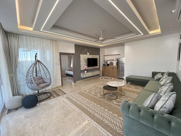 A modern living room with a sofa, a hanging chair, a television, and a kitchen area.