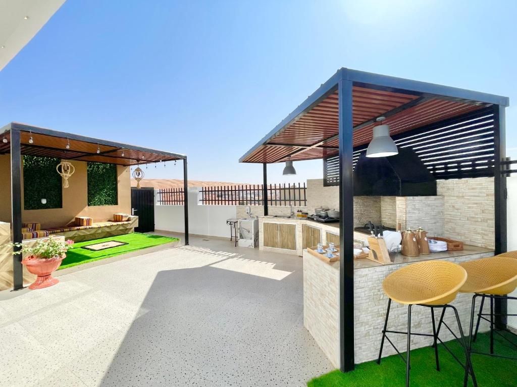 An outdoor patio area with a seating arrangement, a small kitchen setup, and a pergola structure.