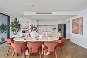 A modern dining area with a round table, six chairs, and a kitchen in the background. - Opulent Designer Escape|Ocean View, Pool & Parking (Palm Beach)