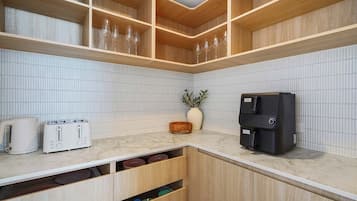 A kitchen with white tiled backsplash, wooden cabinets, a marble countertop, a coffee machine, and two white toasters.