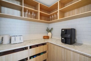 A kitchen with white tiled backsplash, wooden cabinets, a marble countertop, a coffee machine, and two white toasters. - Opulent Designer Escape|Ocean View, Pool & Parking (Palm Beach)