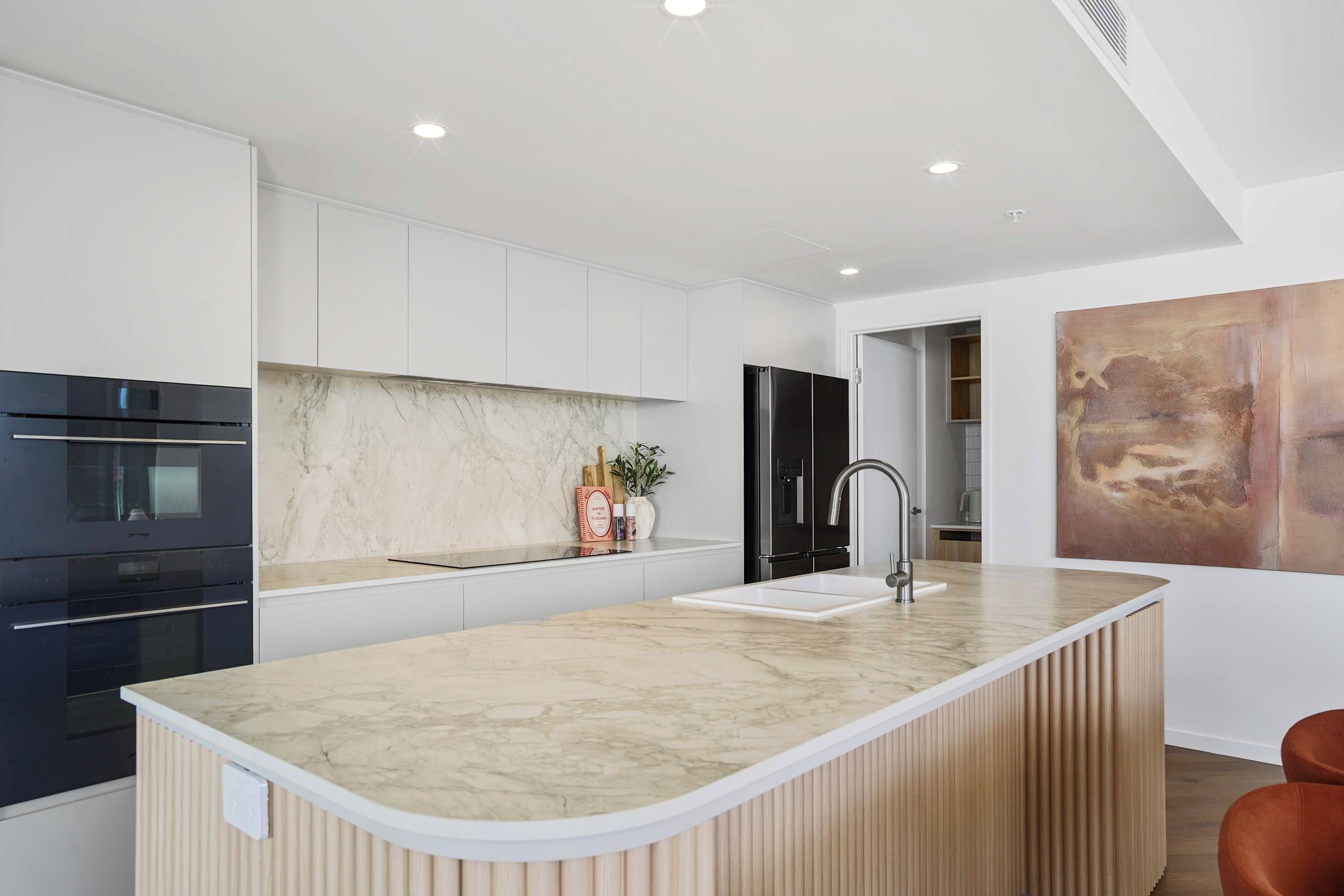 A modern kitchen with a marble countertop, stainless steel appliances, and a wooden island.