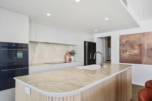 A modern kitchen with a marble countertop, stainless steel appliances, and a wooden island. - Opulent Designer Escape|Ocean View, Pool & Parking (Palm Beach)