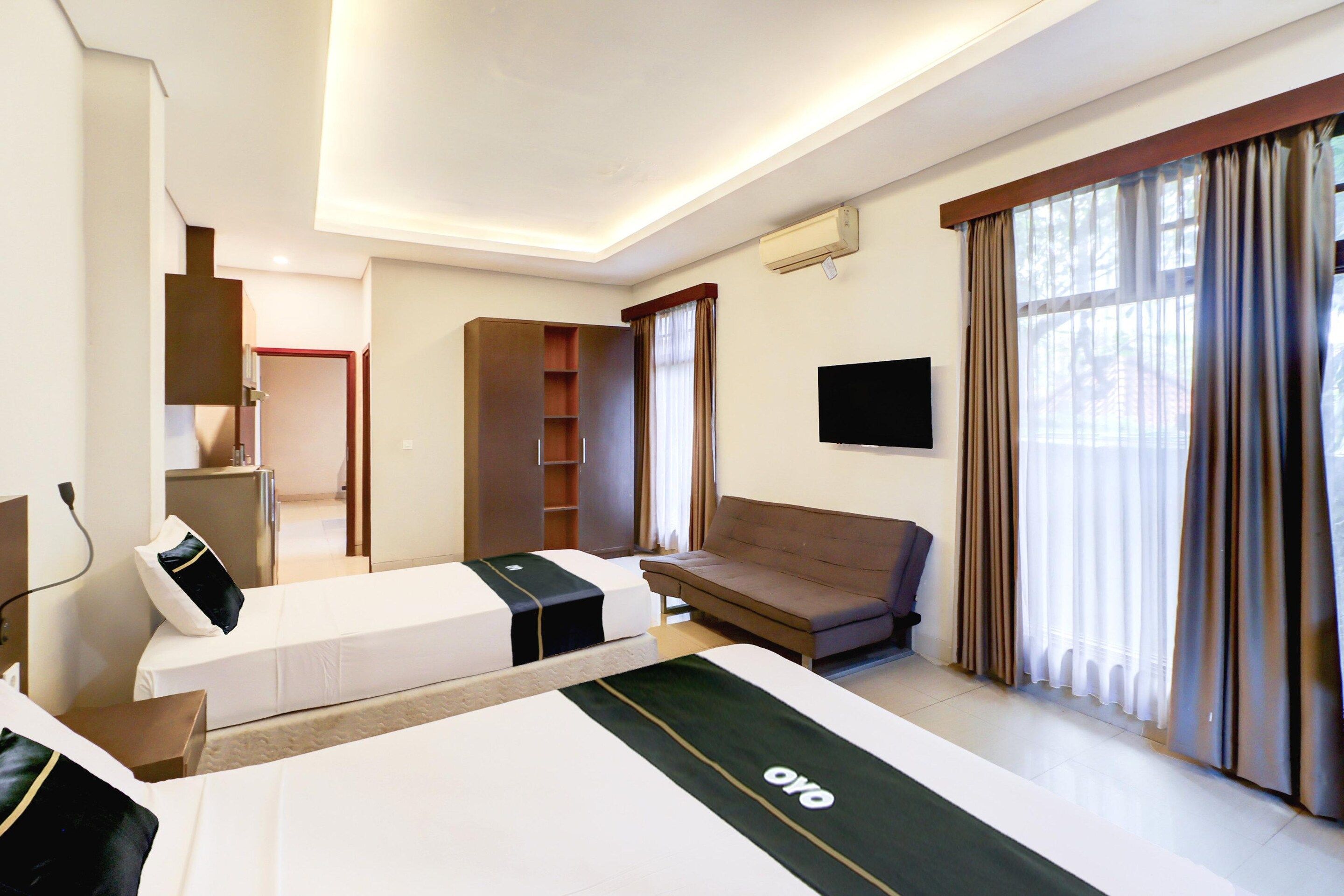 A hotel room with a bed, a sofa, a TV, a wardrobe, and a window with curtains.