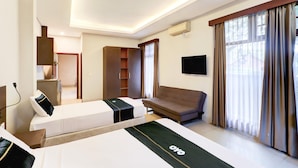 A hotel room with a bed, a sofa, a TV, a wardrobe, and a window with curtains. - Spacious Family Suite With Free Wifi and Parking (Denpasar)
