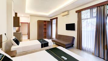 A hotel room with a bed, a sofa, a TV, a wardrobe, and a window with curtains.