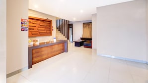 A hotel reception area with a wooden reception desk, a staircase, and a seating area with a sofa and armchairs. - Spacious Family Suite With Free Wifi and Parking (Denpasar)