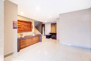 A hotel reception area with a wooden reception desk, a staircase, and a seating area with a sofa and armchairs. - Spacious Family Suite With Free Wifi and Parking (Denpasar)