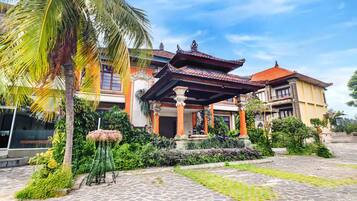 A traditional building with a tiled roof, a covered entrance, and a garden with palm trees and plants.